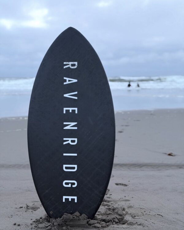 Black carbon fiber Raven Ridge skimboard standing in the sand at the beach